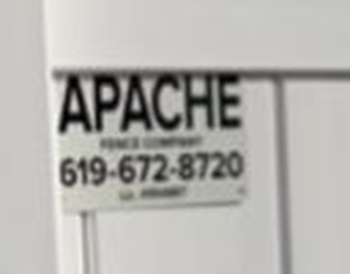 Apache Fence job sign reading APACHE Fence Company 619-672-8720 mounted on a finished white vinyl fence