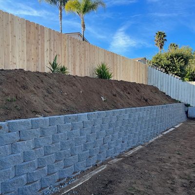 Long block retaining wall topped with new fencing along a graded slope