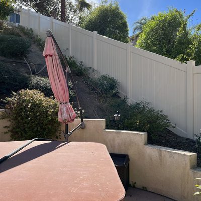 Sandstone vinyl privacy fence along a hillside patio and retaining wall