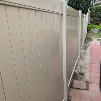 Sandstone vinyl privacy fence stepping up a landscaped slope