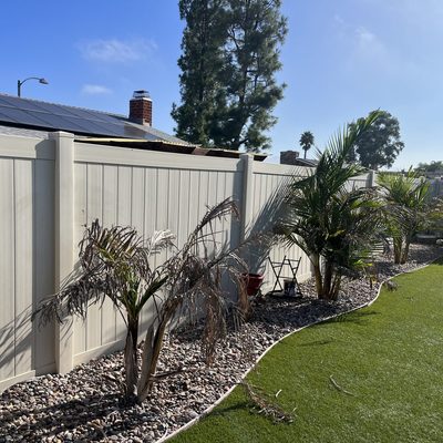 Tan vinyl privacy fence behind a drought-tolerant yard with palms and gravel