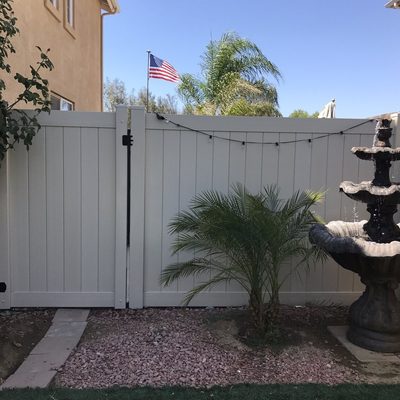 White vinyl double drive gate beside a palm and fountain in a front yard