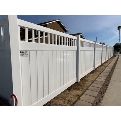 White vinyl privacy fence with open lattice top along a sidewalk, with the Apache Fence job sign attached