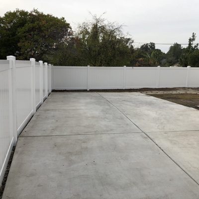 White vinyl privacy fence enclosing a new concrete pad and yard