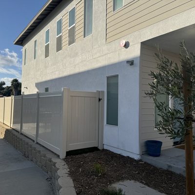 White vinyl privacy fence and gate in a narrow side yard between homes